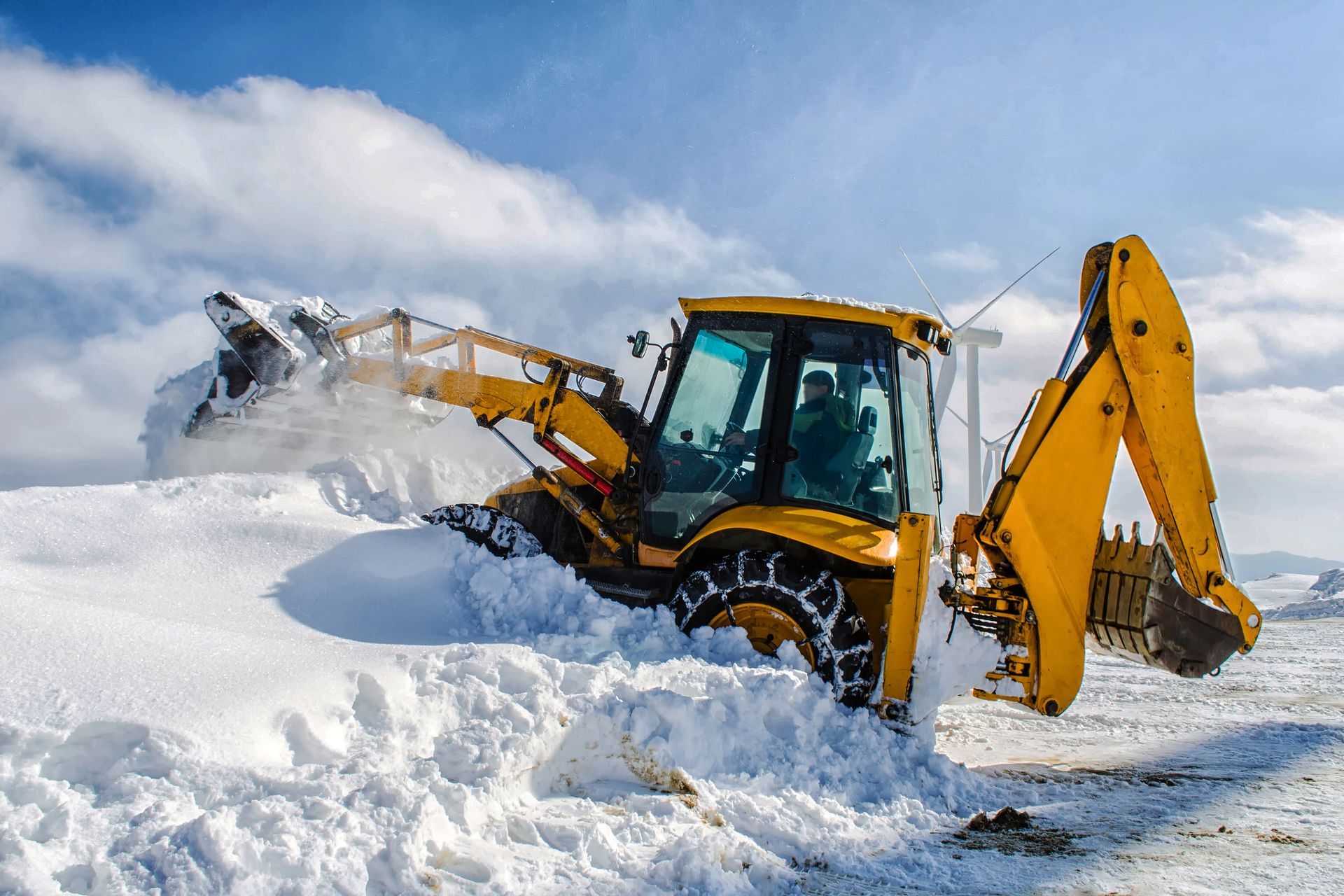 A yellow excavator is clearing snow from a road.
