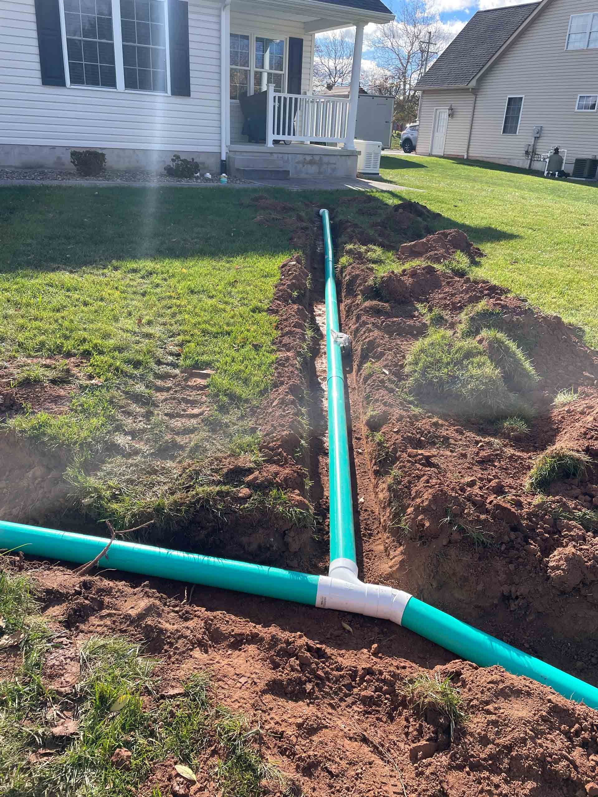 A green pipe is being installed in the dirt in front of a house.