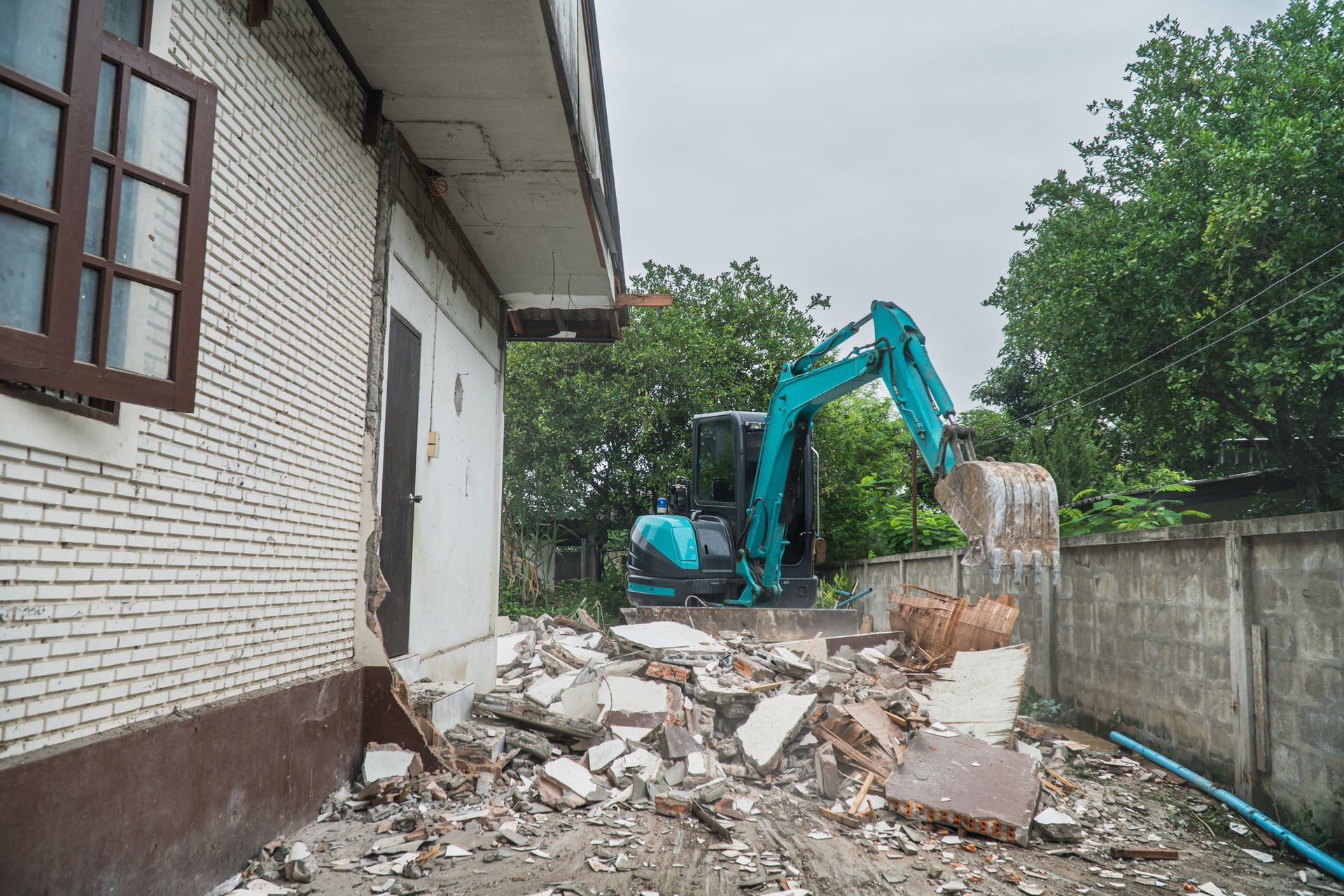 A blue excavator is demolishing a brick building.