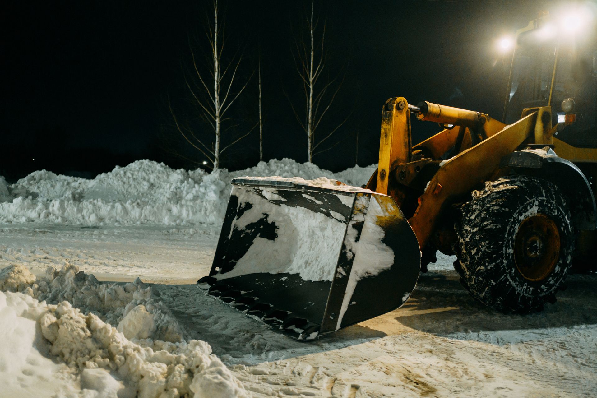 A snow plow is clearing snow from a parking lot at night.
