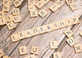 Scrabble tiles spelling “LEADERSHIP” on a wooden surface with scattered letter tiles
