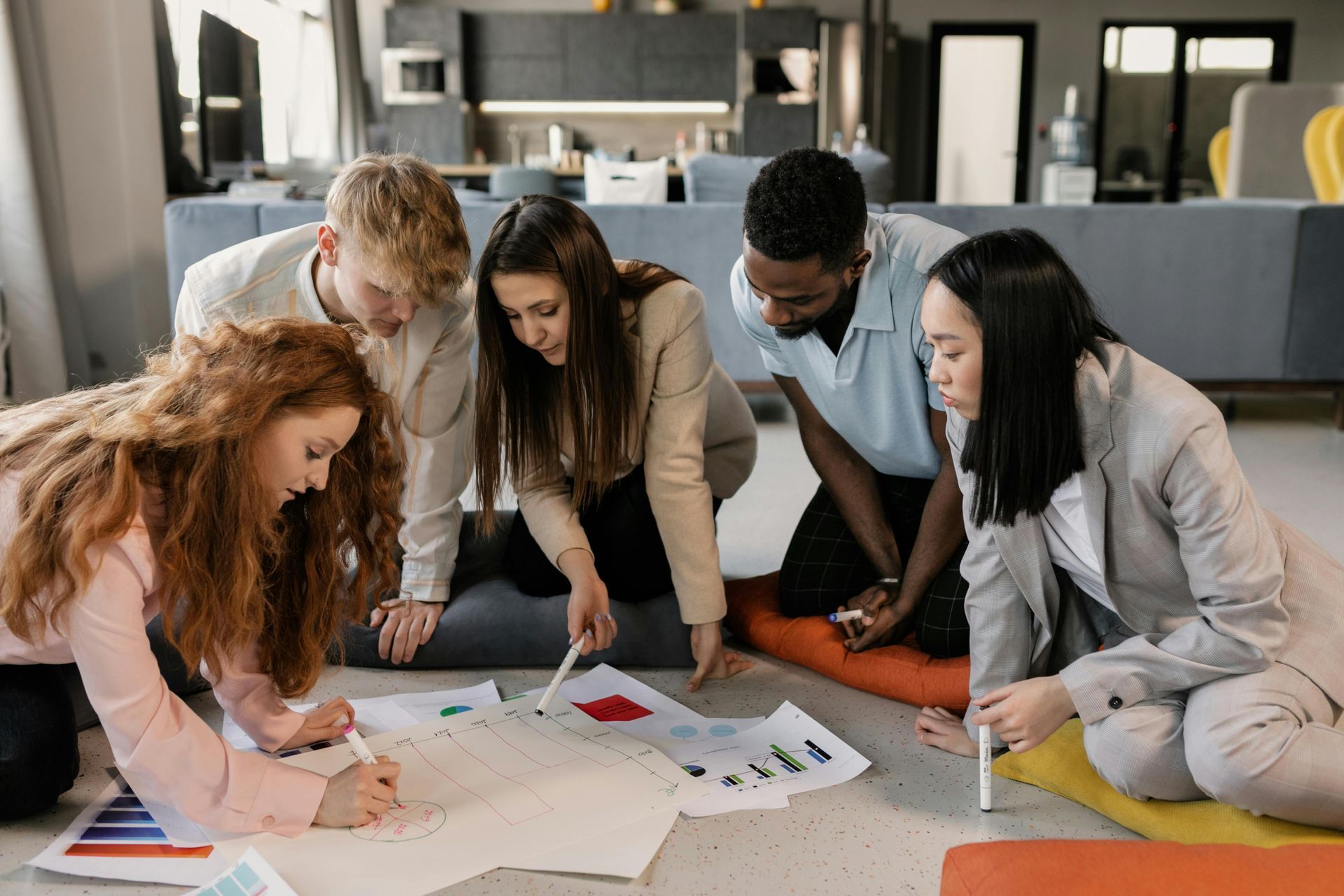 Five people collaborating on papers and charts in a bright office lounge