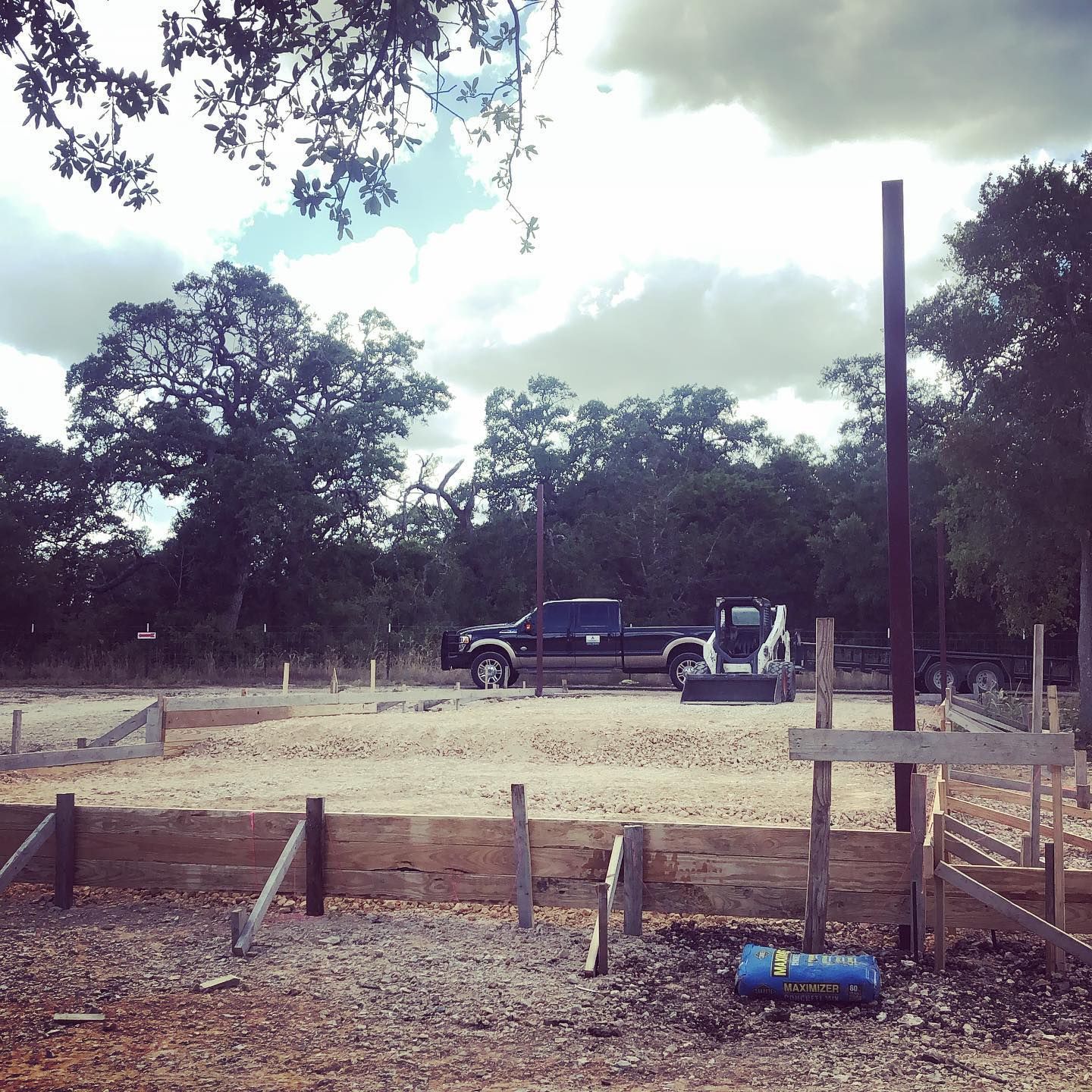 Construction site with wooden forms, a truck, and equipment under a cloudy sky.