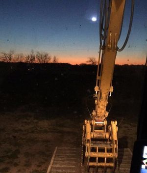 Yellow excavator arm against a dusk sky with moon.