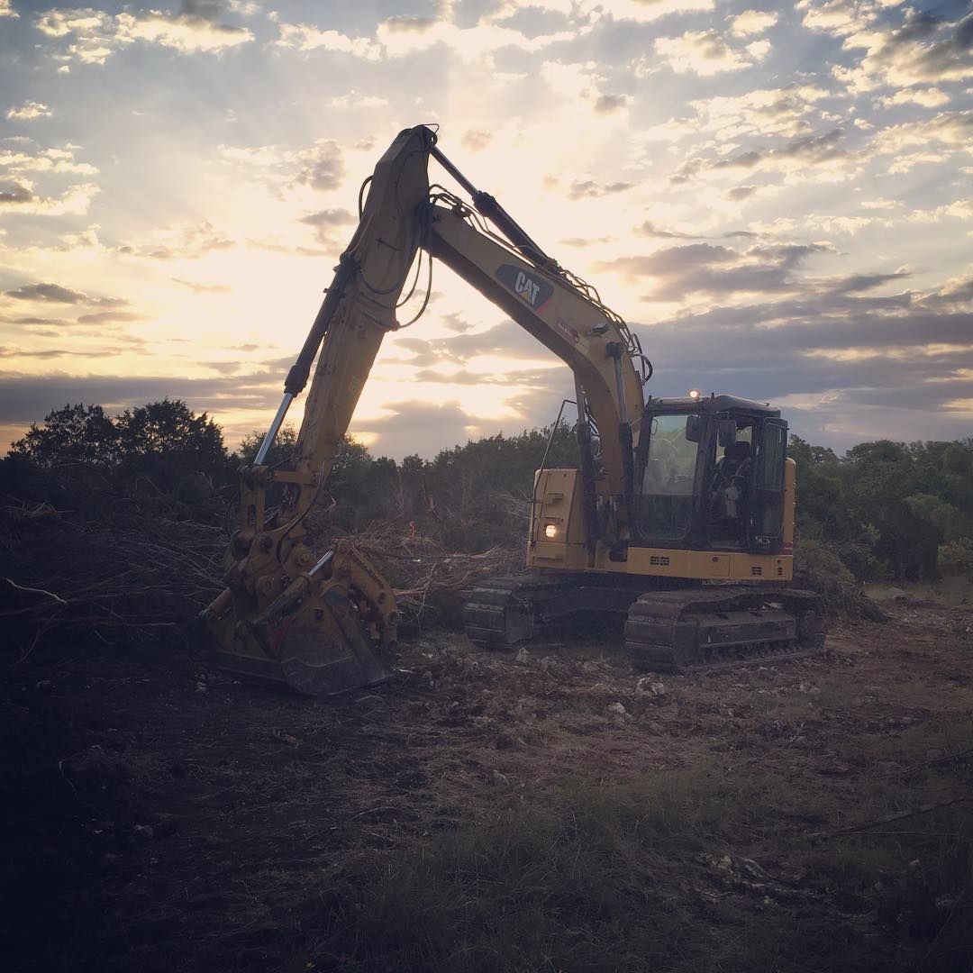 Yellow excavator in field at sunset, digging up debris with trees in the background.