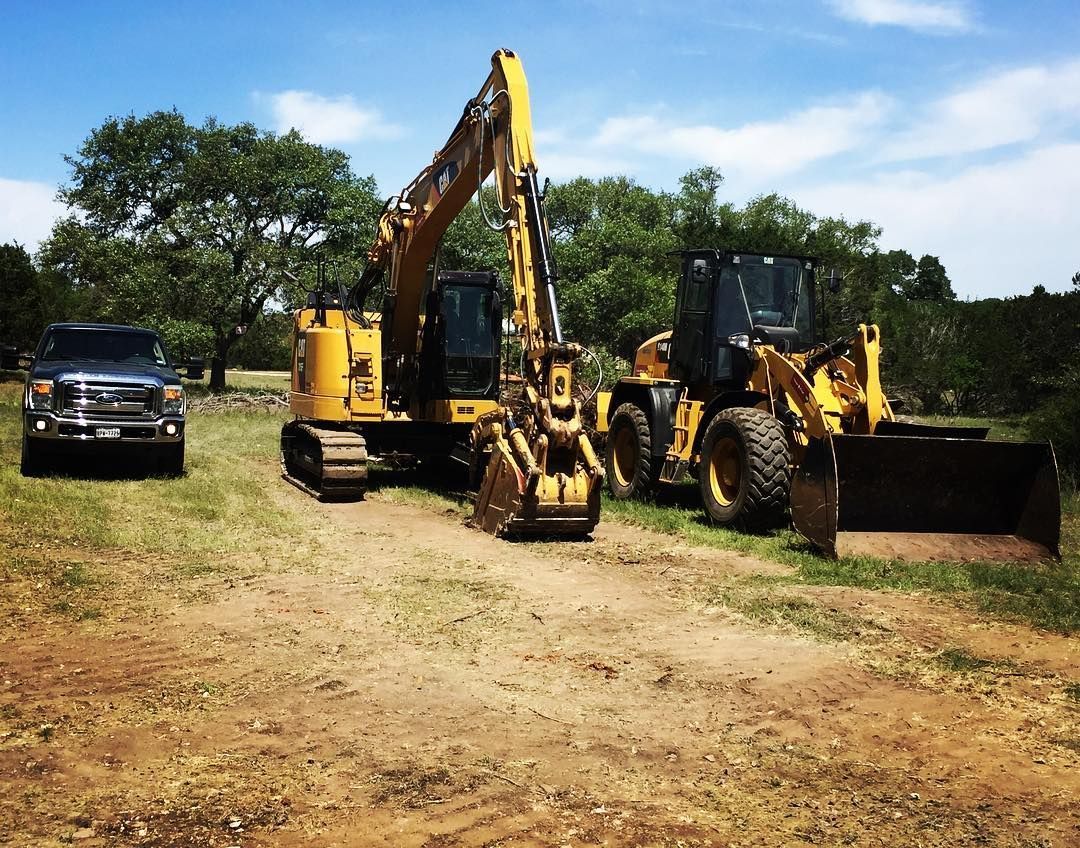 Yellow excavator and loader parked on dirt, with a black truck nearby.