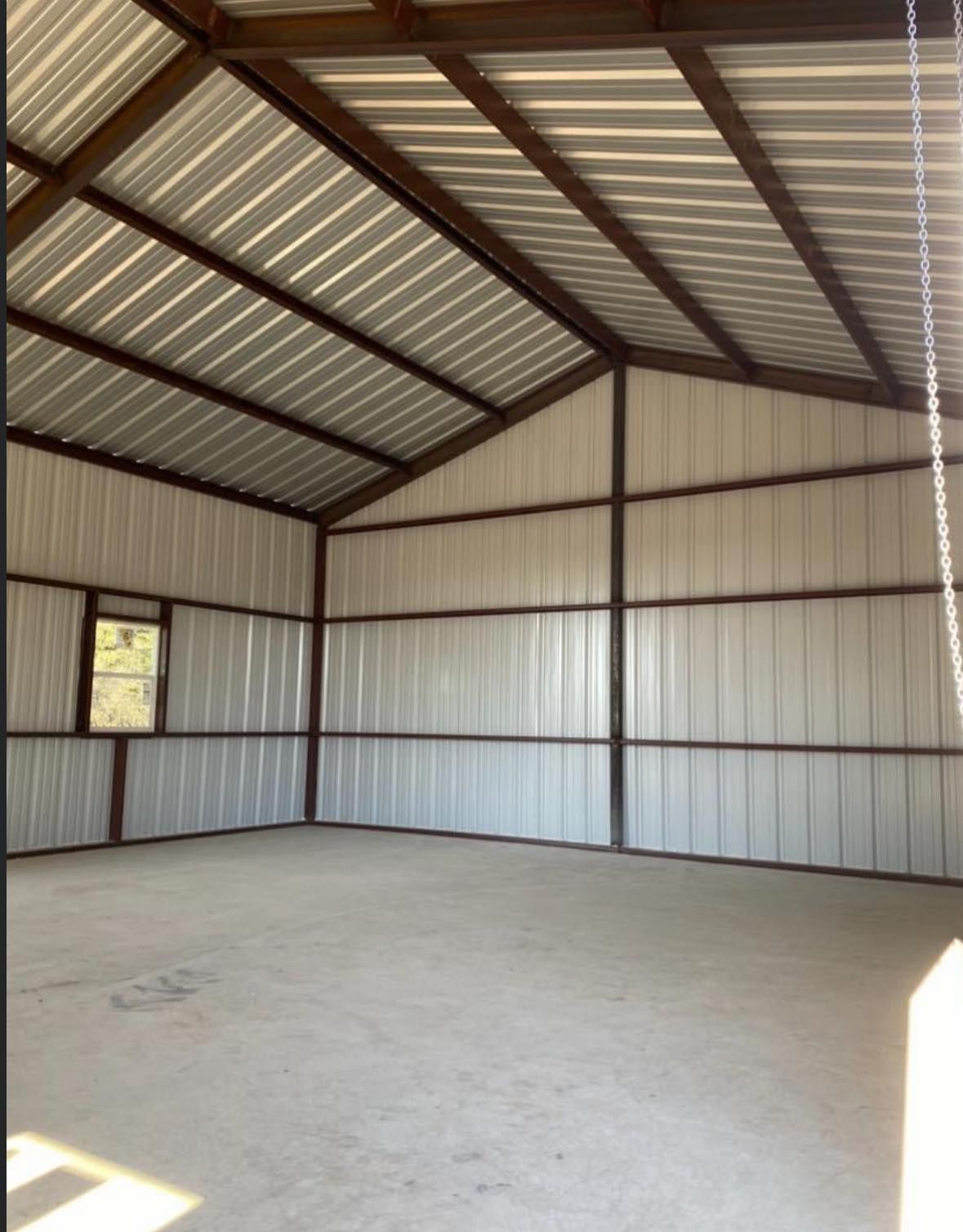 Interior of a metal building with a concrete floor, walls, and ceiling, with a window visible on the left wall.
