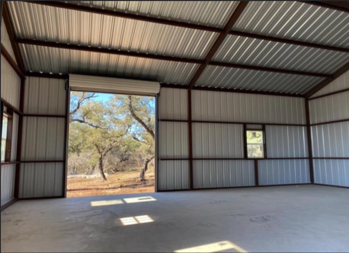Interior of a metal building with an open doorway revealing trees and sunlight.