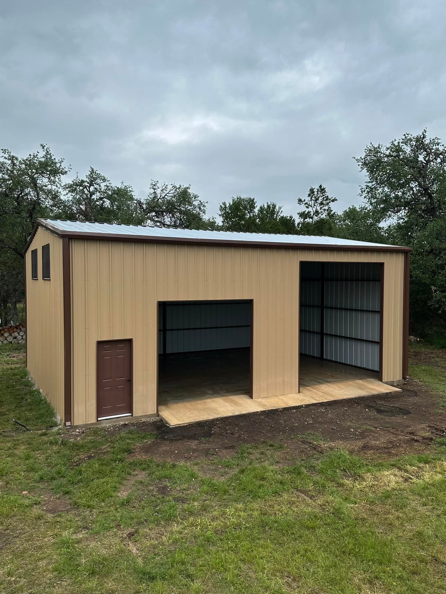 Tan metal storage building with open bay and small side door, set in grassy area.