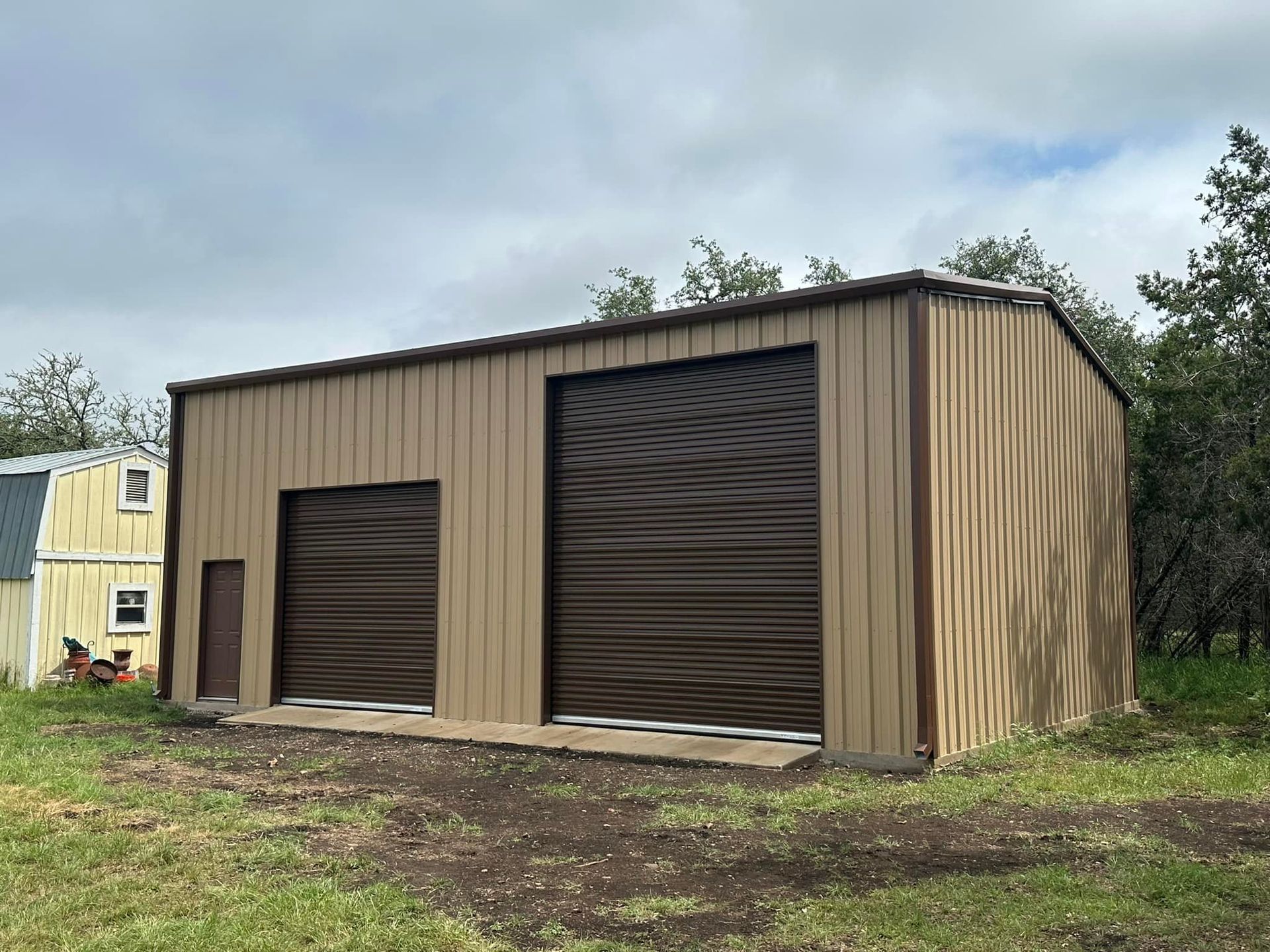 Tan metal garage with two brown roll-up doors, brown trim, and a small side door; outdoors.