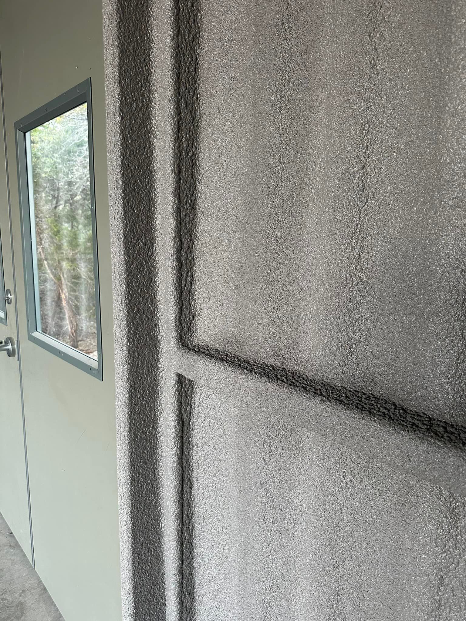 Close-up of a textured, light gray wall with a black stripe, and a doorway with a window.