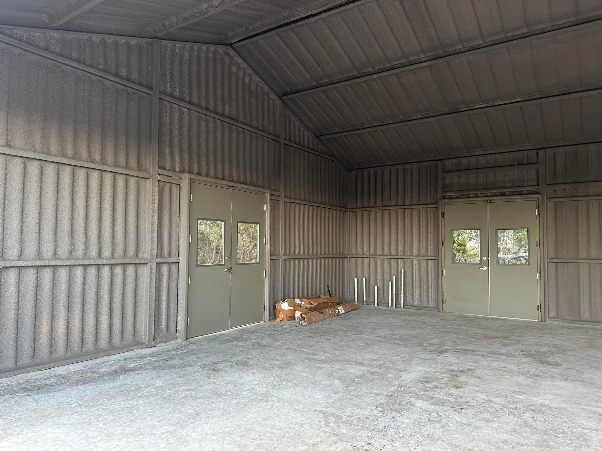 Interior of a grey metal shed with two matching doors, gravel floor, and corrugated walls and roof.