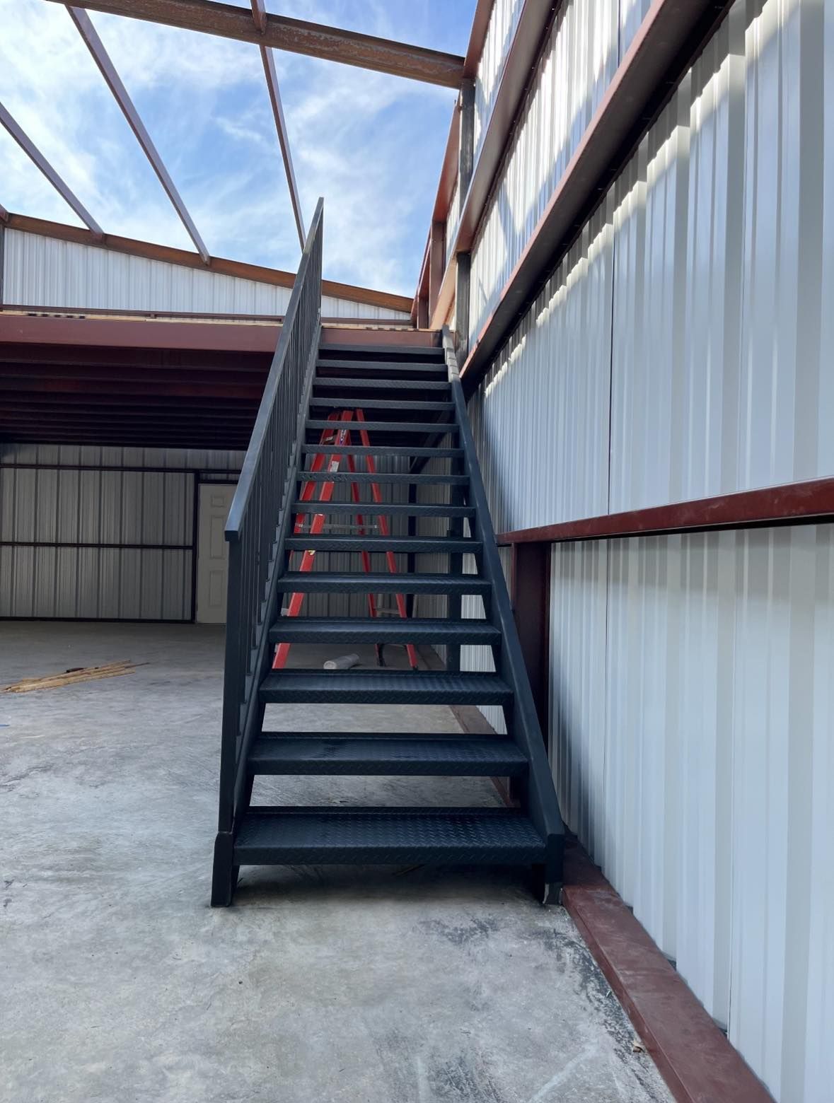 Black metal stairs leading upwards inside a building with a corrugated metal wall.