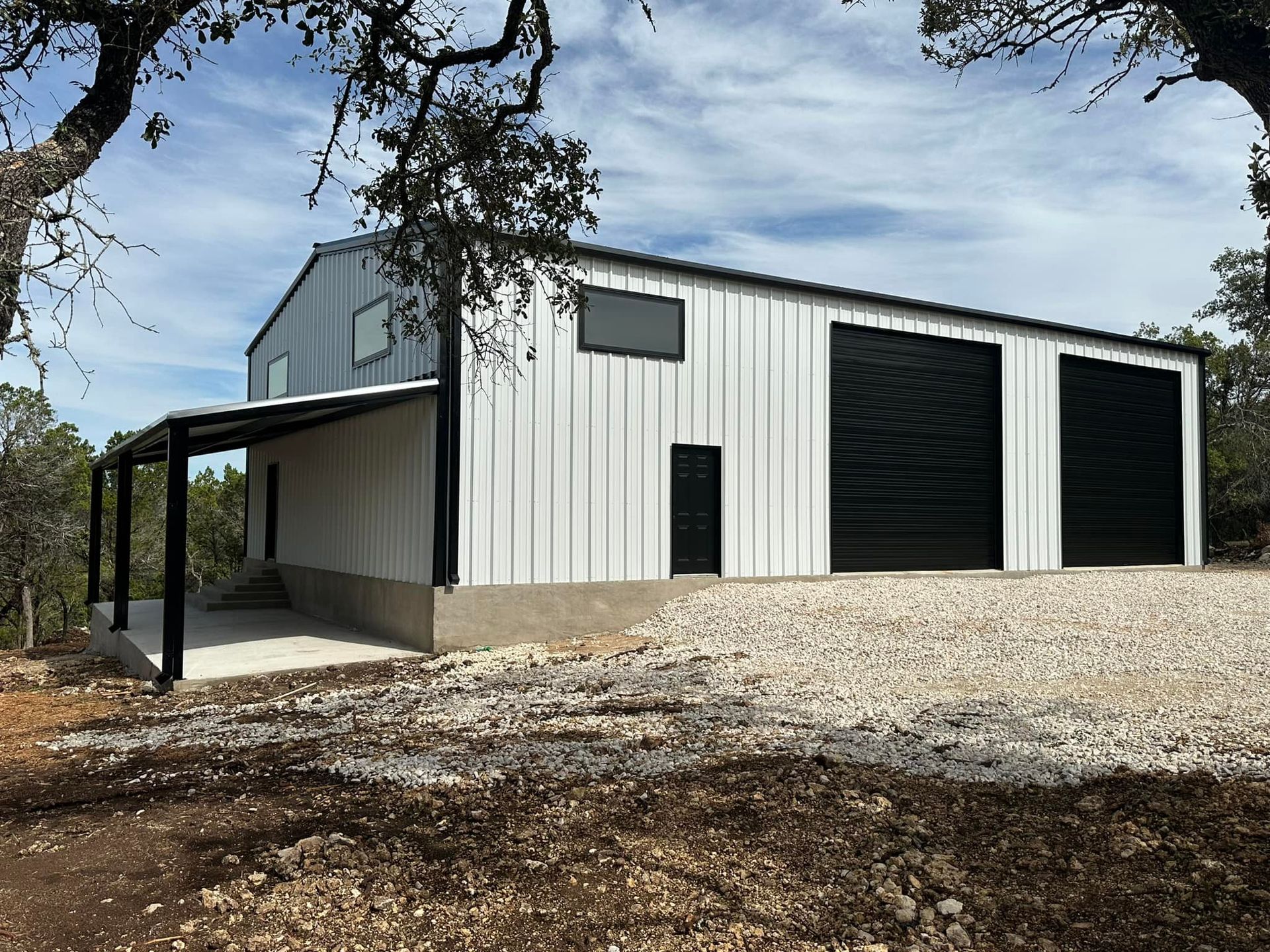 White metal barn with black garage doors, awning, and trim, on a gravel base.