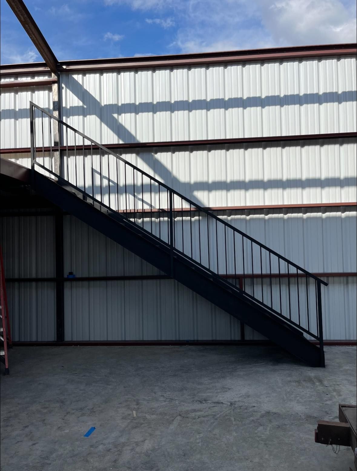 Black metal staircase inside a building with a corrugated metal wall and concrete floor.