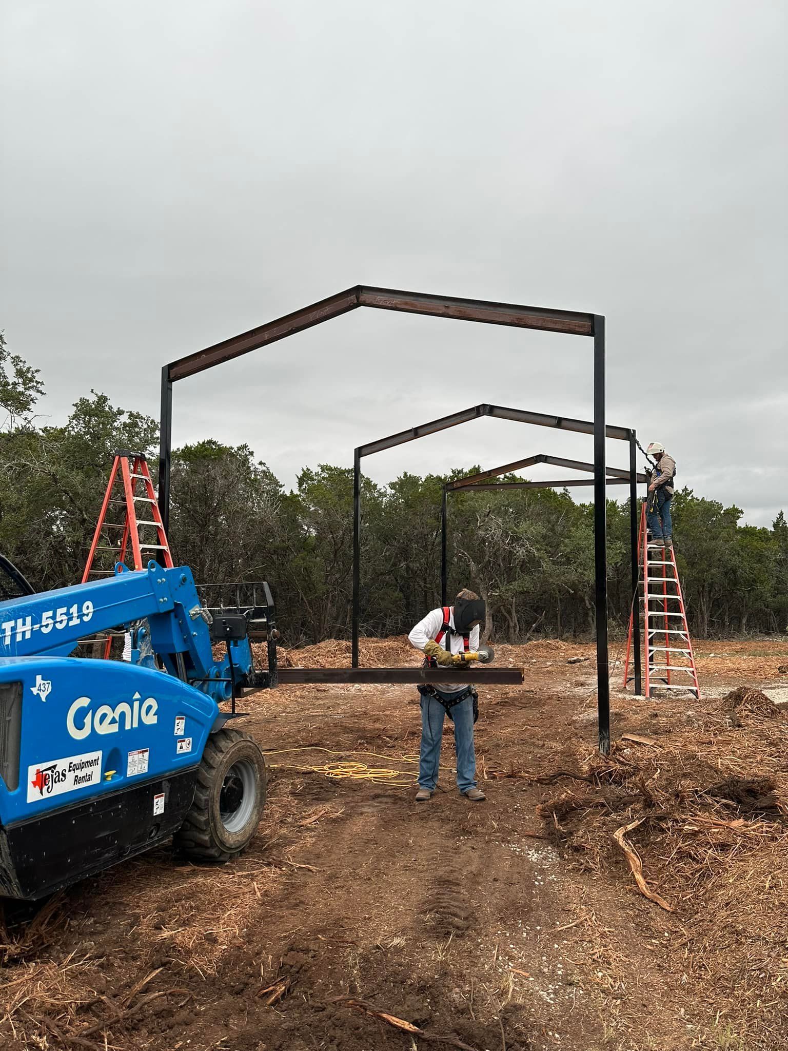 Construction workers building a steel frame structure outdoors on a cloudy day. A Genie lift is present.