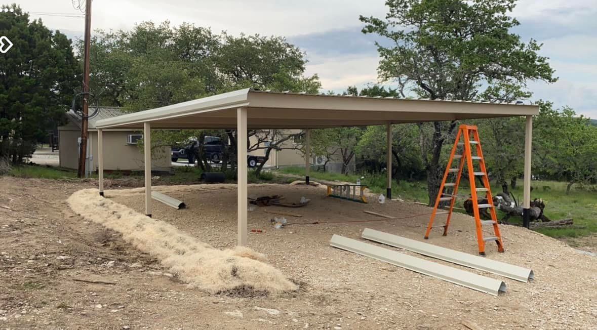 Carport with metal roof; beige, open-air structure. Ladder and building materials nearby on gravel.