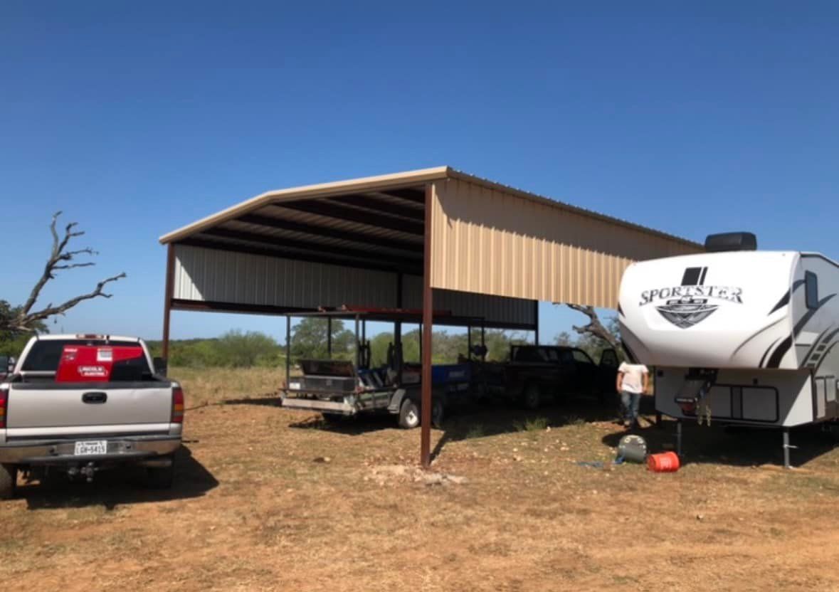 A metal carport shades a truck, golf cart, and camper on a sunny, grassy lot.