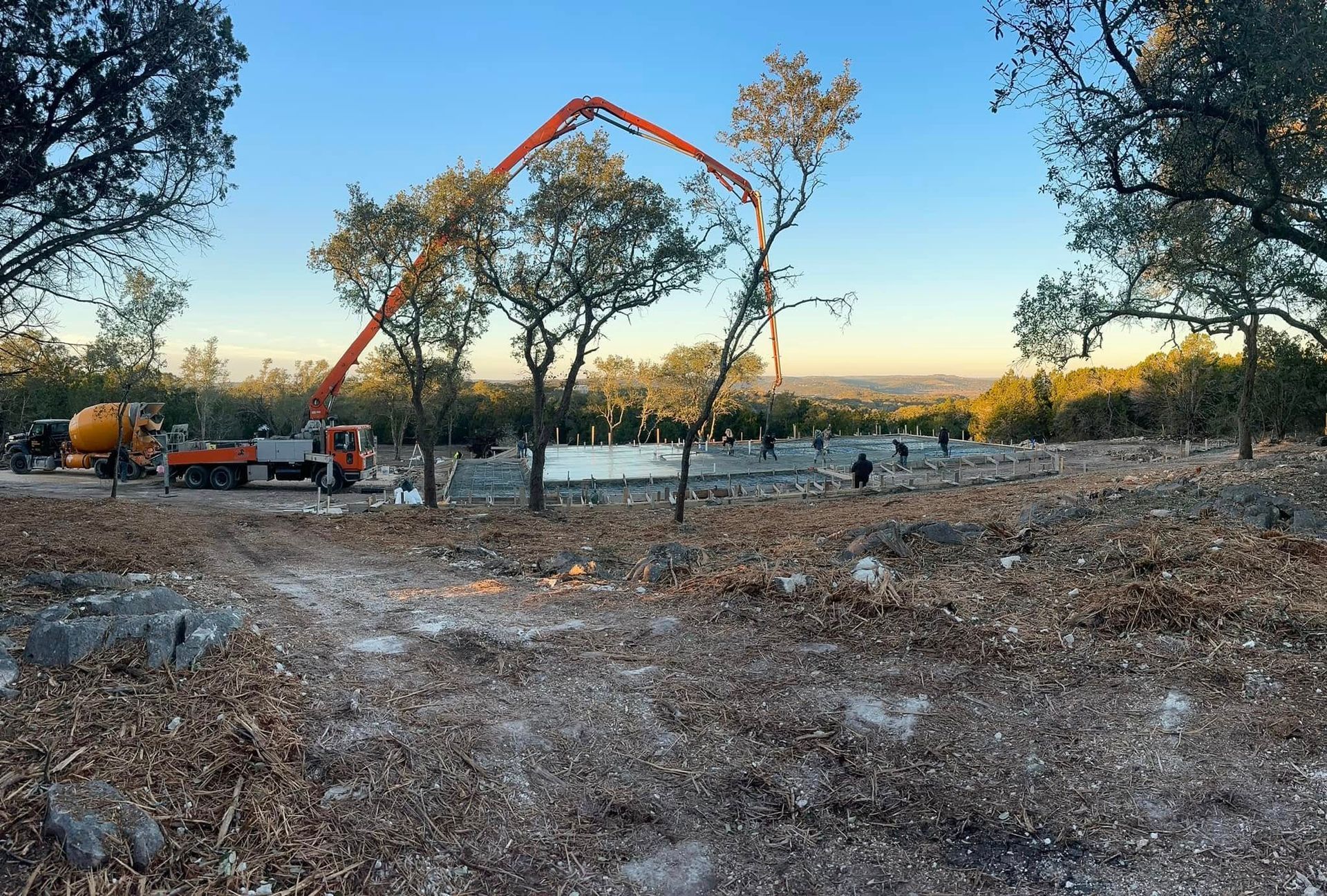 Concrete being poured at a construction site by a boom truck, trees in background, sunny day.