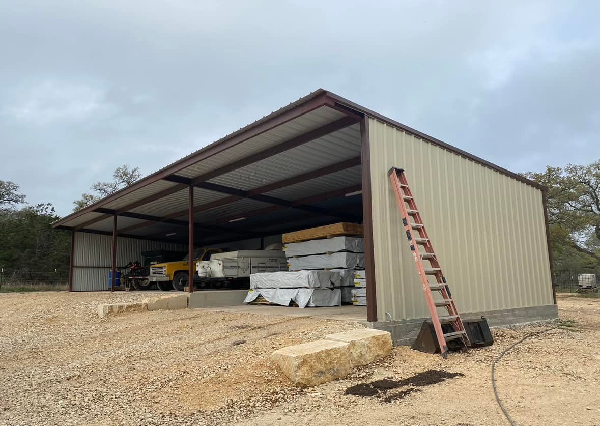 Metal shed with stacked lumber and a ladder, set on a gravel lot under a cloudy sky.