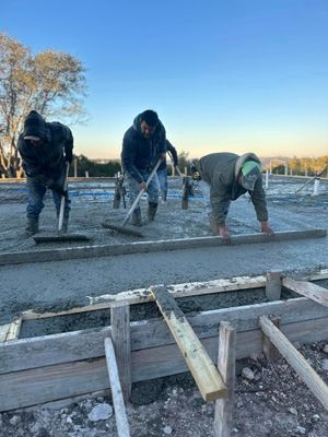 Workers leveling wet concrete with tools at a construction site.