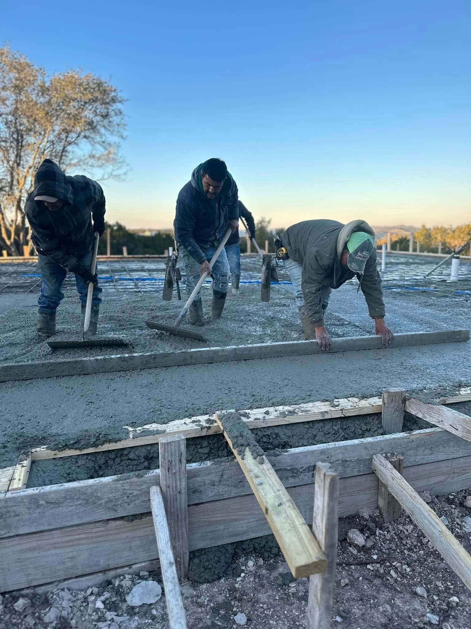 Construction workers leveling concrete with tools outdoors.