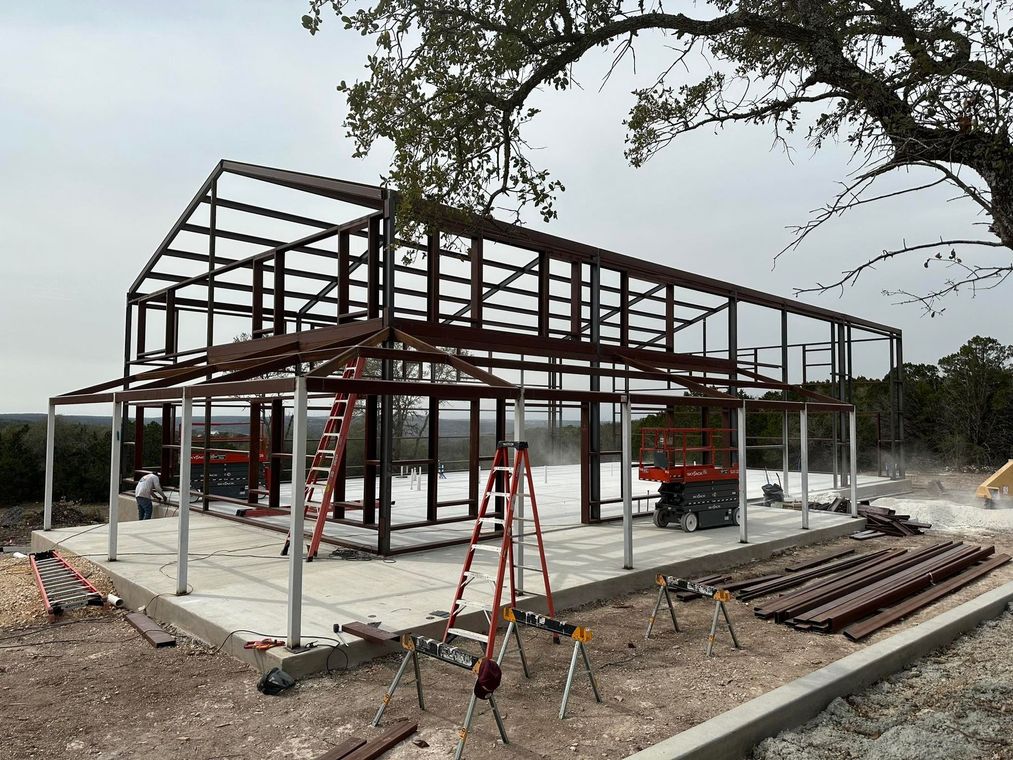 Steel frame building under construction on concrete foundation outdoors.