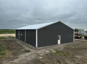 Gray metal warehouse building with white trim, door, and roof, set on a concrete foundation in a field.