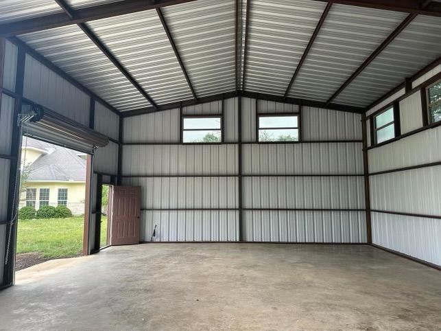 Interior view of a metal building with a concrete floor, windows, and an open garage door.