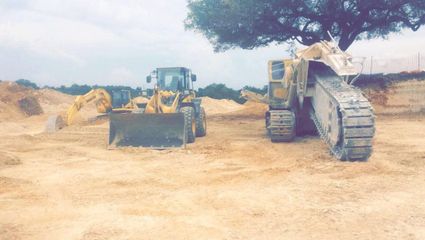 Yellow construction equipment on a sandy worksite under a cloudy sky.