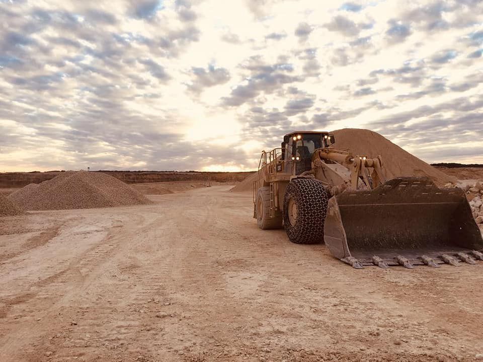 Wheel loader at a construction site, near a pile of gravel, under a cloudy sky.
