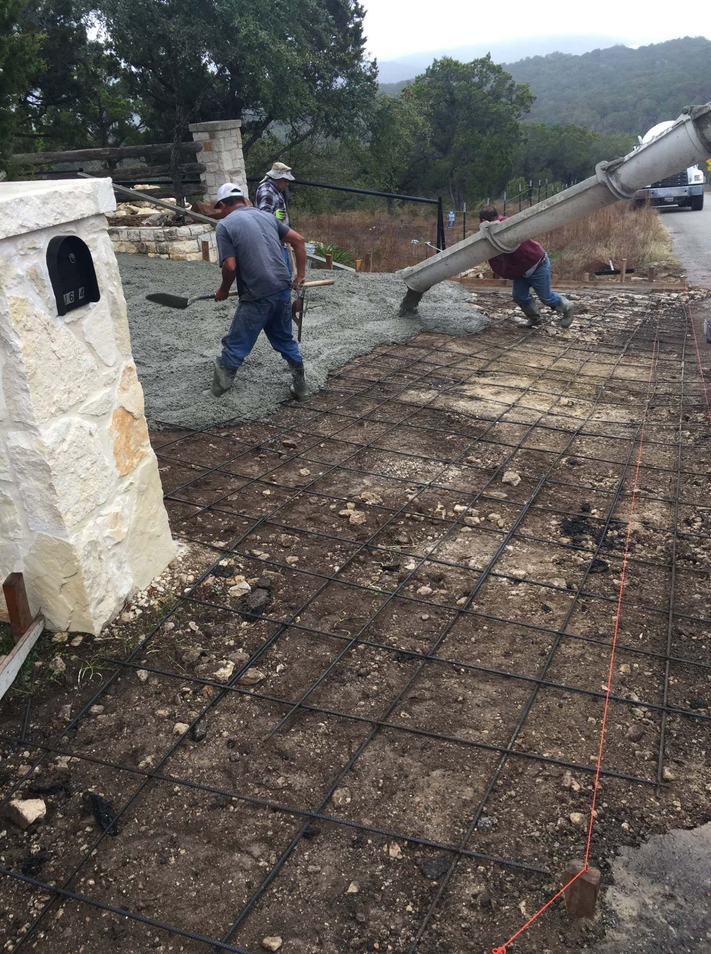 Workers pouring concrete at a mailbox post on a driveway.