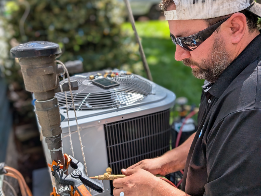 Full Time Heating & Cooling | A man is working on an air conditioner outside.