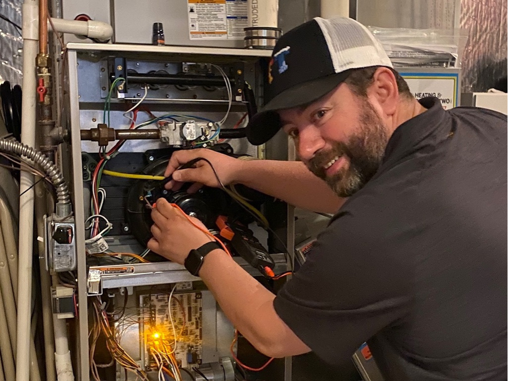 Full Time Heating & Cooling | A man is working on a heating system in a basement.