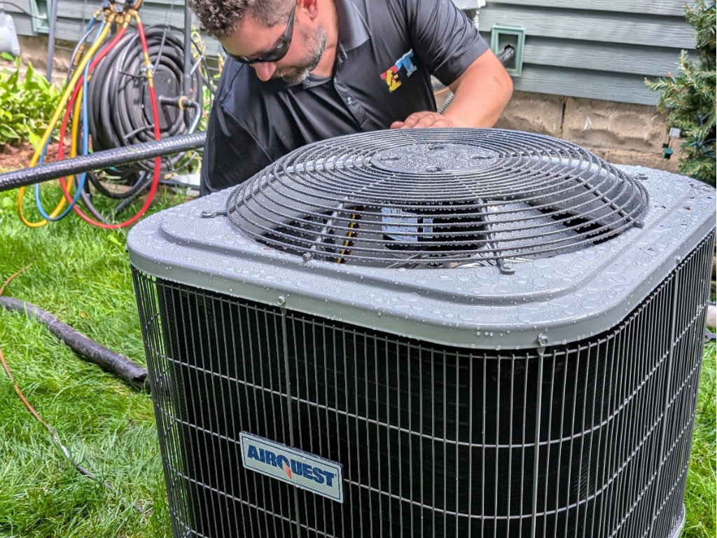 Full Time Heating & Cooling | A man is working on an air conditioner outside of a house.