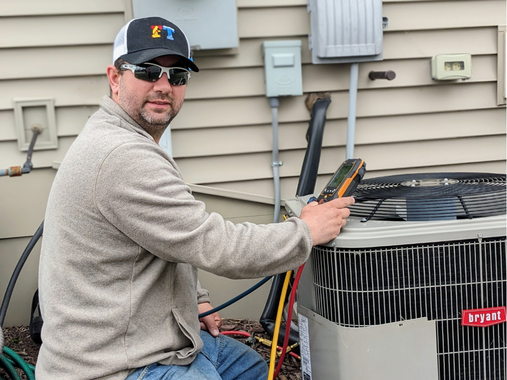 Full Time Heating & Cooling | A man is sitting on the ground working on an air conditioner.