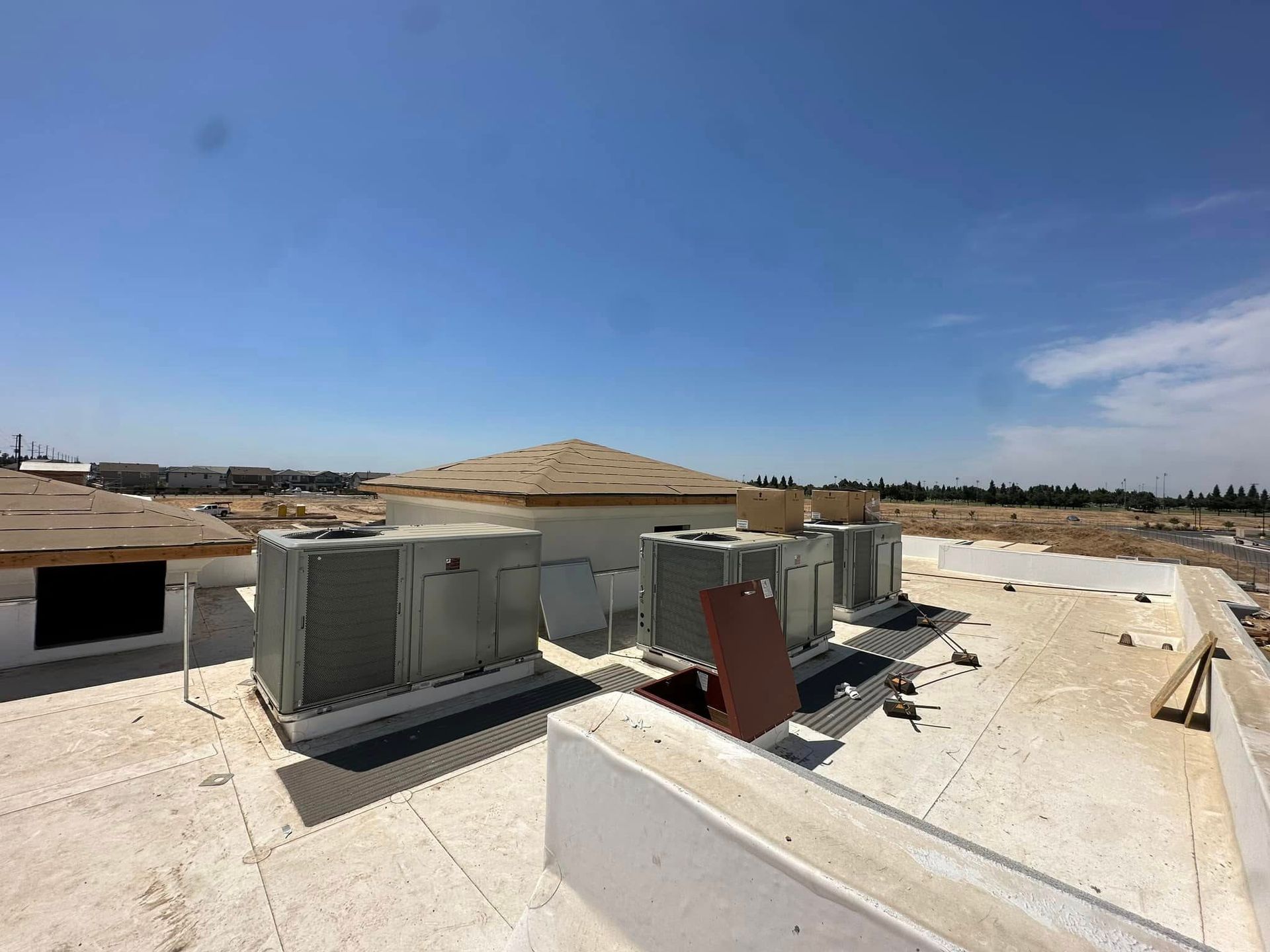 Rooftop with HVAC units under a clear blue sky, buildings in the distance.