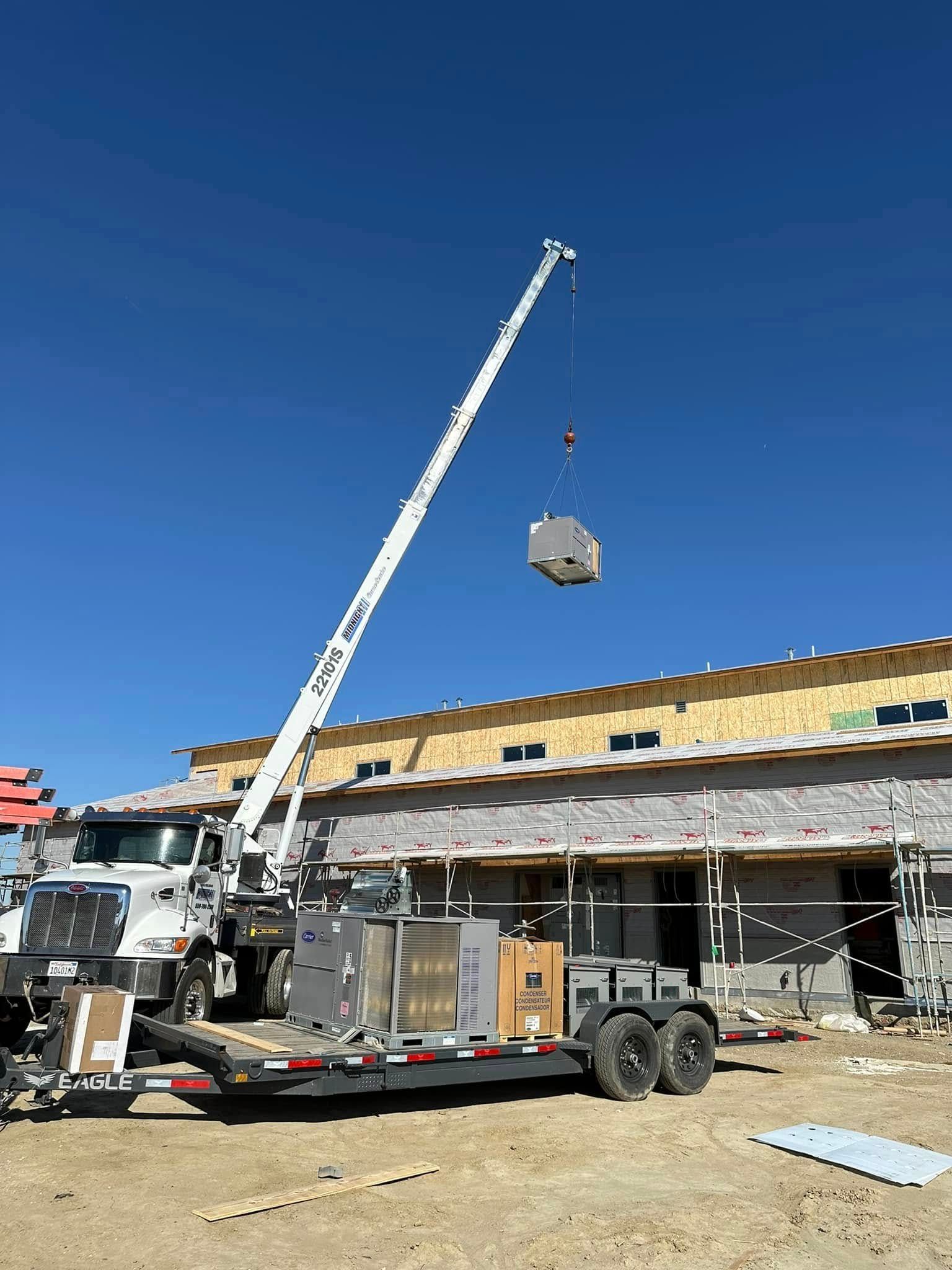 Crane lifting an HVAC unit at a construction site on a sunny day.