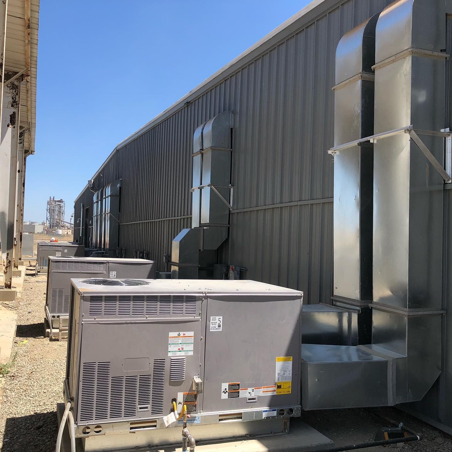Air conditioning units and ductwork along a corrugated metal building wall.