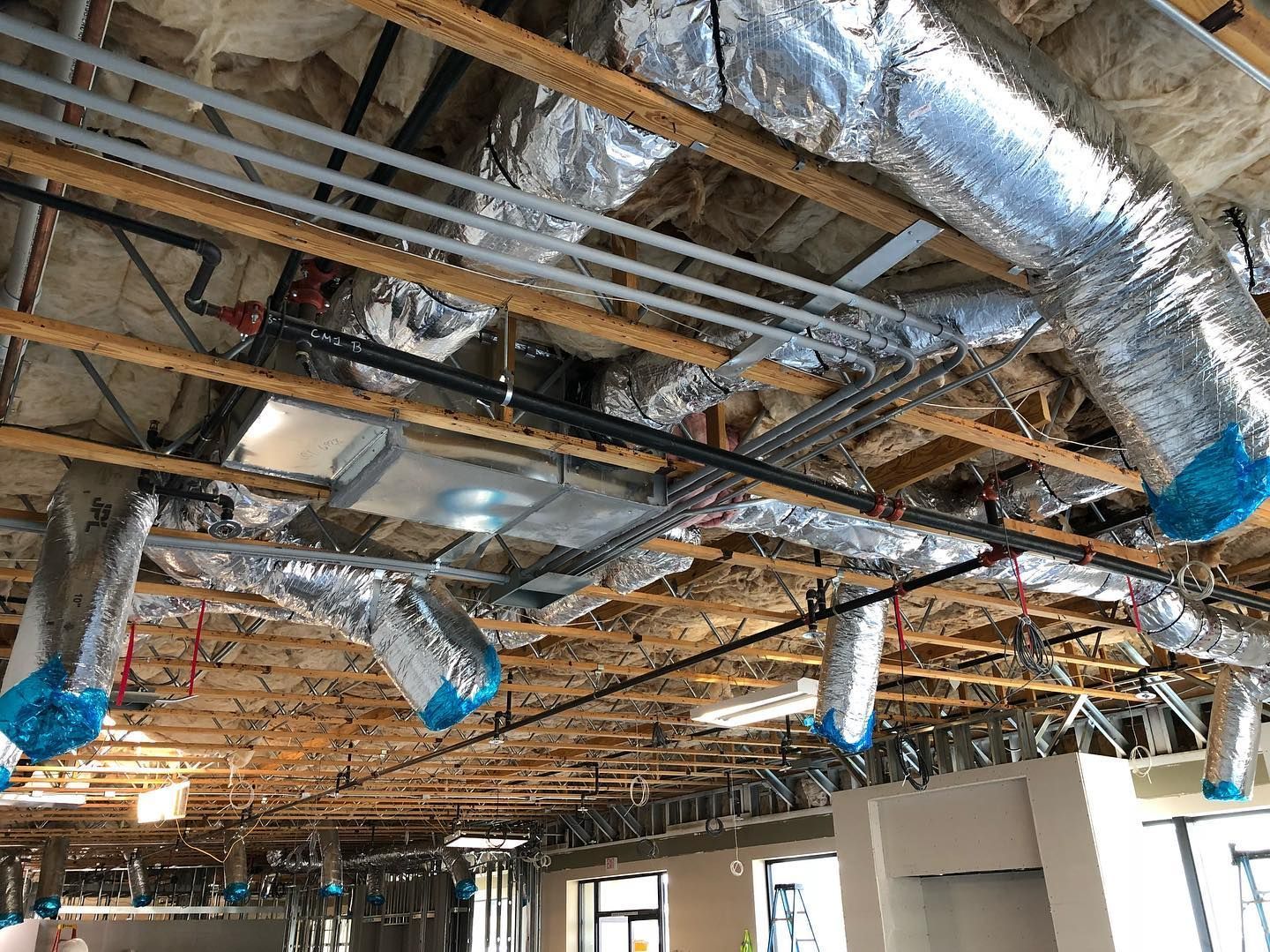 Ceiling under construction: ductwork, pipes, and wiring are visible. Insulation and framing are also present.