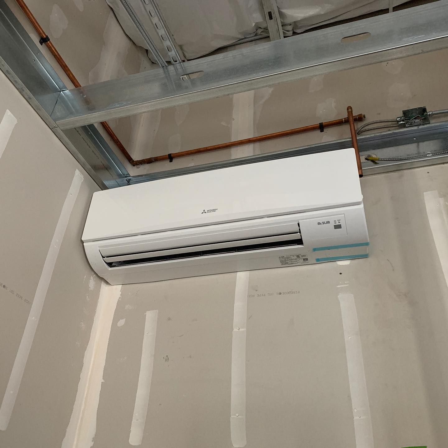 White air conditioning unit installed on a wall with copper pipes running above it.