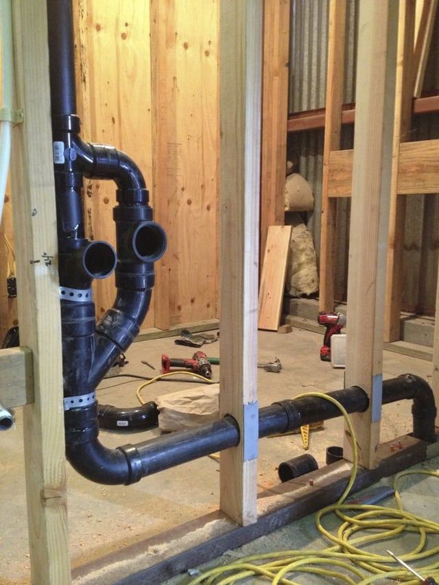 Black plumbing pipes installed in a wooden framed wall. Tools and a yellow cord are nearby.