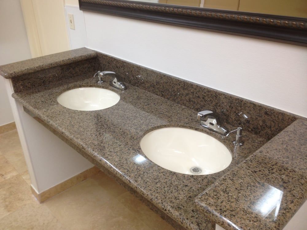Bathroom with two white oval sinks in a brown granite countertop, chrome faucets, and a mirror above.