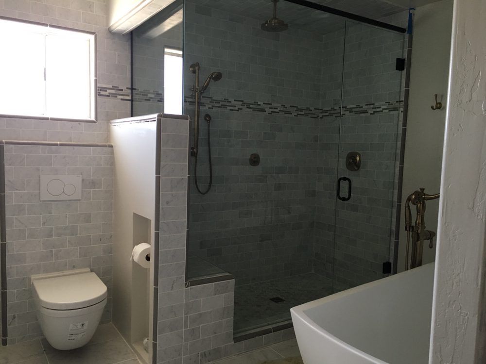 Modern bathroom with glass shower, toilet, and bathtub; gray tile.