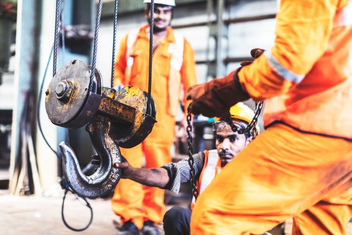 Workers in orange coveralls connecting a large hook in a factory setting.