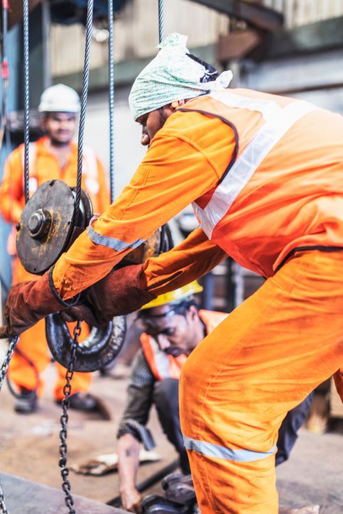 Close-up of a man in orange overalls performing crane repair service, alongside a couple of workers