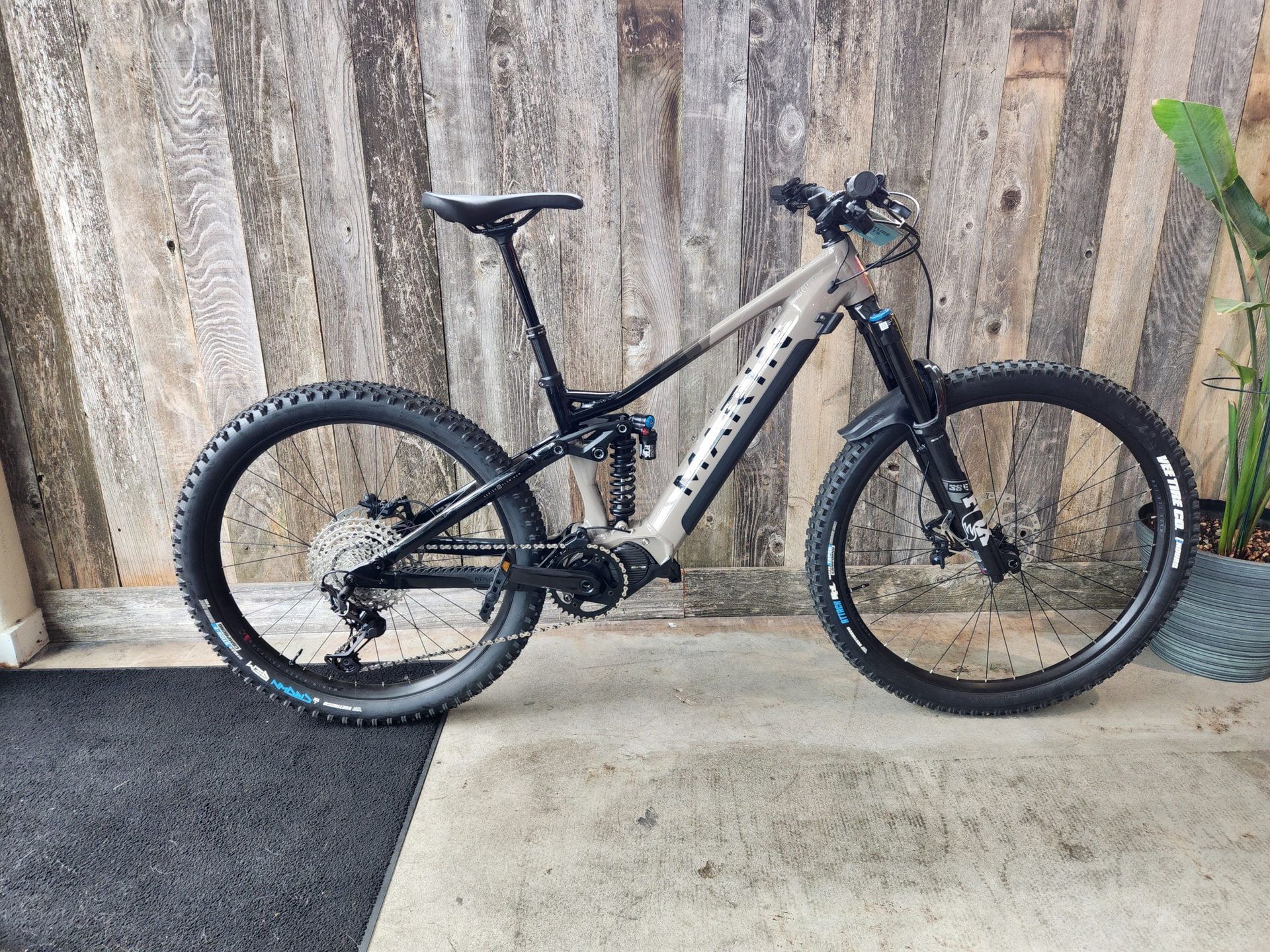 A mountain bike is parked on a sidewalk in front of a wooden wall.