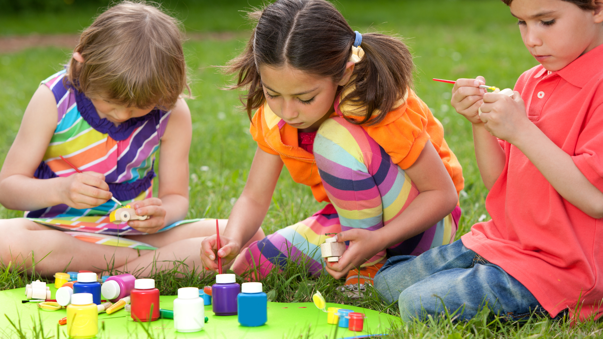 Children painting outdoors on a grassy lawn, using colorful paints.