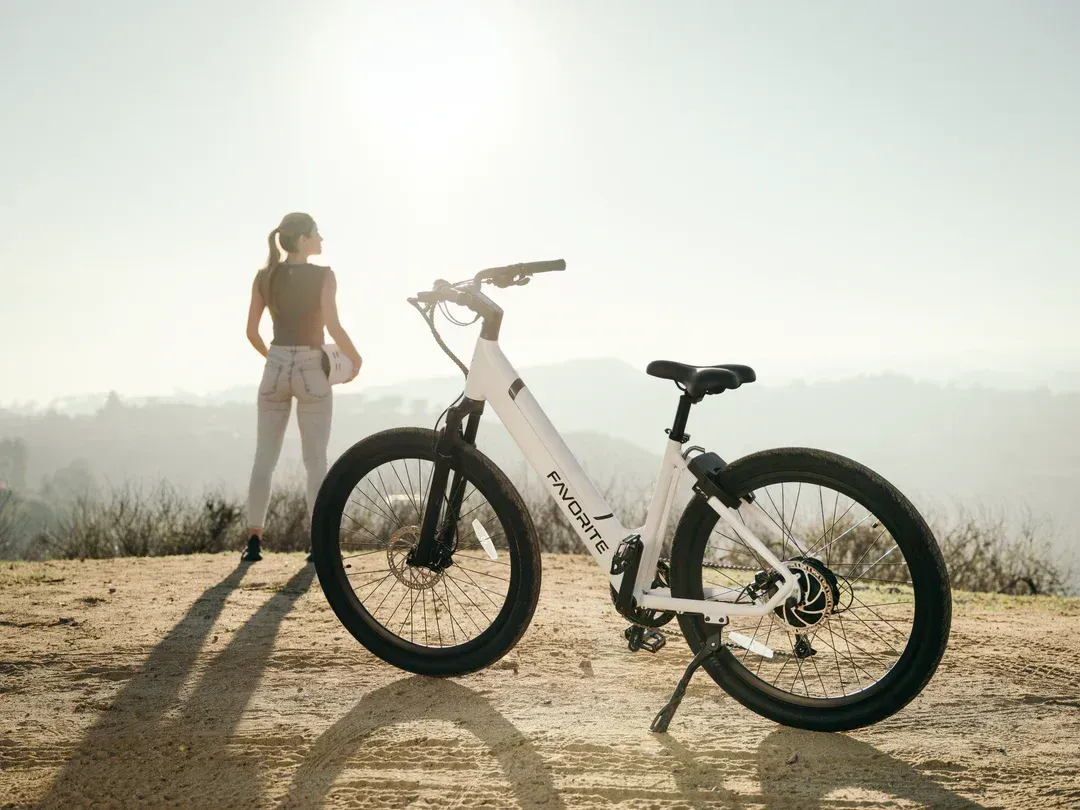 A woman is standing next to a white bicycle on top of a dirt hill.