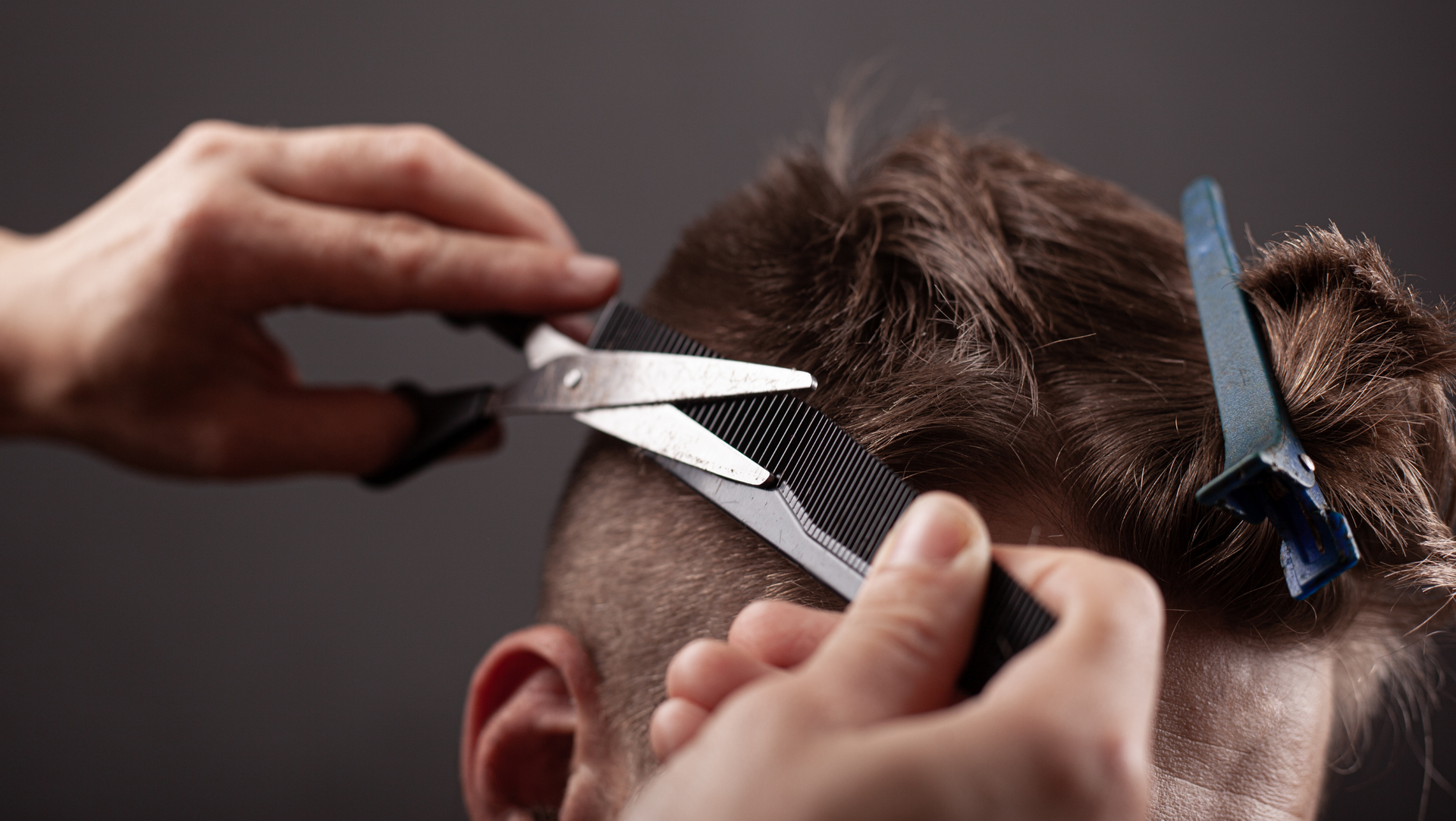 A man is getting his hair cut by a barber with scissors and a comb.